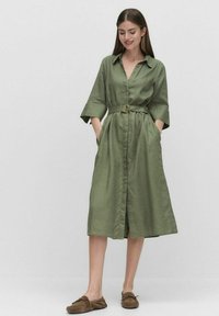 Zielona sukienka do kolan z kołnierzykiem, zapinana na guziki, z paskiem w talii i bocznymi kieszeniami; wykonana z lekkiego materiału o gładkiej fakturze.
