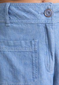 Light blue denim shorts featuring a single back pocket, button closure, and a smooth texture. The fabric shows a subtle woven pattern.