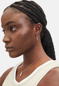 Zilveren creolen met een sleutelhanger, gedragen bij een lichtgekleurde, mouwloze top met een ronde hals en een geribbelde textuur. Vlecht van zwart haar.