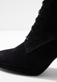 Botín negro de ante hasta el tobillo con punta afilada, diseño con cordones y detalles de costura sutiles, que cuenta con una textura suave y una silueta elegante.