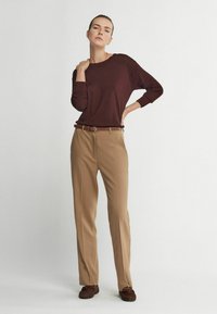 Burgunderröd långärmad tröja kombinerad med beiga högmidjade byxor och bruna skor. Outfiten har en enkel, skräddarsydd design.