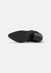 Botín negro de ante hasta el tobillo con punta afilada, suela texturizada y tacón bajo cuadrado. Presenta un diseño minimalista y un acabado suave.