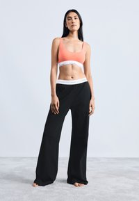 Kora sporta krūšturis ar baltu Calvin Klein jostu, apvienots ar melniem platām biksēm ar līdzīgu zīmola jostu.