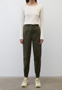 Weißes Langarmhemd mit feinen braunen Streifen, kombiniert mit olivgrünen Hose mit elastischem Bund und hellen Sneakers.