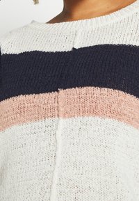 Sweter z dzianiny z poziomymi paseczkami w kolorze granatowym, pudrowym i kremowym. Okrągły dekolt, strukturalna tkanina oraz widoczne detale szwów.