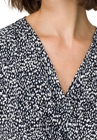 Tissu à motif noir et blanc présentant un design en V, avec de petites formes irrégulières créant une apparence texturée.