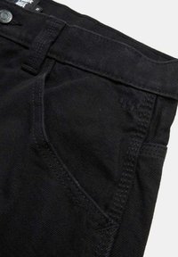Pantalones de mezclilla negra con una textura suave, diseño estándar de cinco bolsillos y costuras en contraste a lo largo de los bordes.