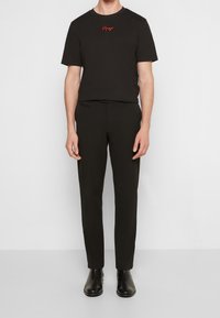 Svart t-shirt med röd logotyp på bröstet, matchad med svarta slim-fit byxor och svarta läderankelstövlar. Enkelt, monokromatiskt outfit.