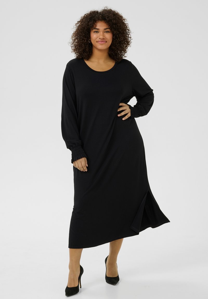 Vestido negro de manga larga con escote redondeado, puños fruncidos, detalle de abertura lateral y corte holgado, confeccionado en una tela suave.