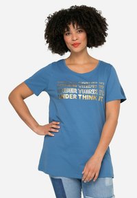 Camiseta de algodón azul con mangas cortas y escote en forma de barco. Presenta texto metálico dorado: "DONE LO PIENSES" en diferentes tamaños y estilos.