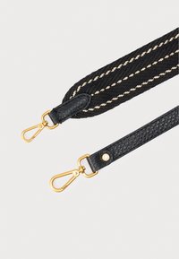 Crni pleteni platneni remen s kremastim prugama, kožnim krajevima i kopčama od zlatnog metala. Teksturirani završetak i dekorativni metalni ukrasi.