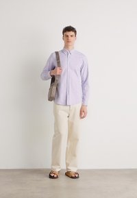 Lichtpaarse overhem shirt, crèmekleurige broeken, bruine sandalen en een grijs schoudertas. Eenvoudig ontwerp met een ontspannen pasvorm.