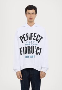 Hvid hætte sweatshirt med stort sort og blåt tekst. Teksten inkluderer "PERFECT FIORUCCI" med legende grafik. Blødt, afslappet design.