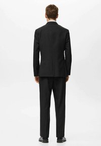 Schwarzer Anzug, einreihige Jacke und passende Hose, glattes Material, keine sichtbaren Muster, normale Revers, flaches Rückendesign, polierte Schuhe.