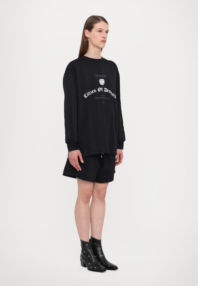 Black oversized sweatshirt with white text, paired with black shorts. The model wears black heeled ankle boots with silver accents.