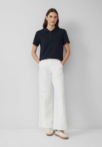 Granatowa koszulka polo z krótkim rękawem i zapięciem na trzy guziki, zestawiona z szerokimi białymi spodniami i beżowymi trampkami z teksturowanymi akcentami.