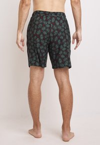 Svarta simshorts med ett mönster av gröna tallar och röda detaljer, elastisk midja, knälång design och ett lätt material.