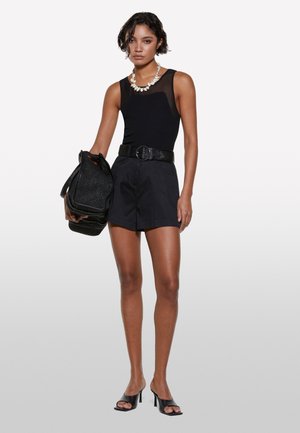 Top nero senza maniche con pannello trasparente, pantaloni corti neri a vita alta, cintura nera con texture, borsa nera e sandali con tacco aperti neri.