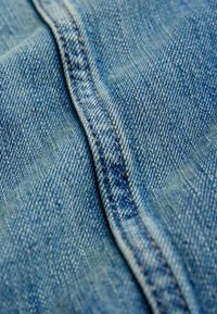 Denim stof in een lichte blauwe tint, met een zichtbare naad met oranje stiksel, die een gestructureerd oppervlak met fijne weefdetails laat zien.