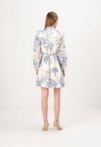 Rochie camizolă cu imprimeu floral în crem, cu detalii albastre. Are mâneci bufante, talie strânsă și tiv evazat. Asortată cu pantofi cu toc nude.