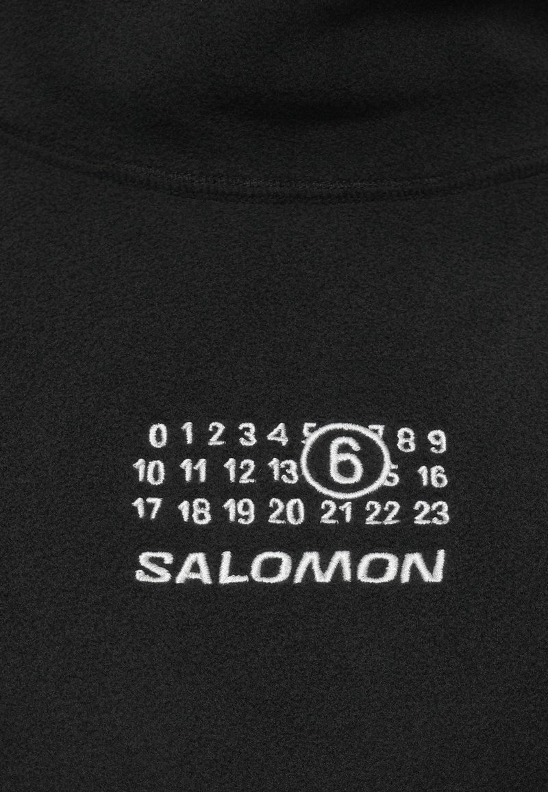 Tejido negro con números impresos en blanco del 0 al 23, con el número 6 enmarcado, y el nombre de la marca SALOMON debajo de los números.