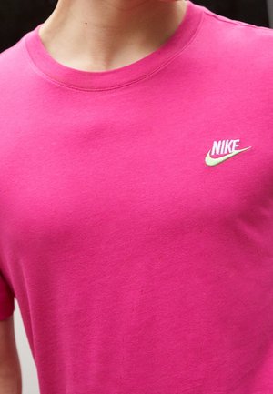 Gros plan d'une personne portant un t-shirt rose vif avec un petit logo Nike blanc et vert sur la partie supérieure gauche de la poitrine.