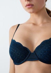 Reggiseno in pizzo blu navy con bordi a scallop, motivi floreali e spalline regolabili, caratterizzato da una finitura liscia e coppe strutturate.