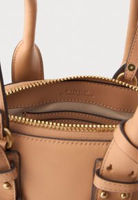 Borsa a tracolla in pelle beige con chiusura a cerniera dorata e dettagli in oro. Presenta due manici corti e un marchio interno visibile sulla fodera in tessuto.