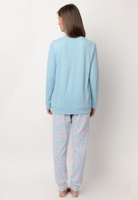 Top de manga larga azul claro con cuello redondo, combinado con pantalones rosa y azul que presentan un patrón de texto repetido. Tejido suave, corte holgado.