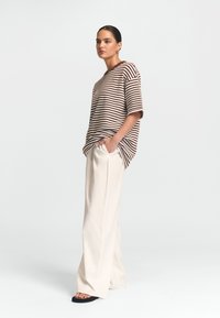 Pruhované hnědé a bílé oversized tričko v kombinaci s krémovými širokými kalhotami a černými sandály, s uvolněným střihem a měkkou texturou.