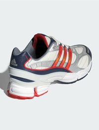 Silberner Sportschuh mit strukturiertem Obermaterial, orange und marineblauen Streifen, Mesh-Futter und einer gepolsterten weißen und roten Sohle.