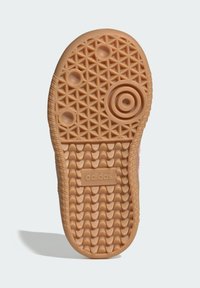 Podeszwa trampka Adidas wykonana z jasnobrązowej gumy, z geometrycznymi wzorami bieżnika i wytłoczonym logo. Okrągłe i owalne detale zwiększają przyczepność.