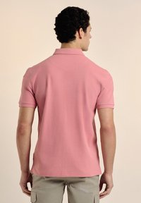 Camisa polo rosa claro de manga corta, con un cuello clásico y una textura suave, mostrada desde la parte de atrás. Diseño minimalista, sin patrones ni acentos.