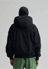Schwarze Kapuzenjacke mit lässiger Passform, gerippten Bündchen und Bund. Glatter Stoff mit minimalistischem Design und dezenten Schulterdetails.