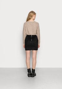 Maglione beige in maglia a maniche lunghe abbinato a una mini gonna nera in suede con zip sul retro. Stivali neri alla caviglia completano l'outfit.