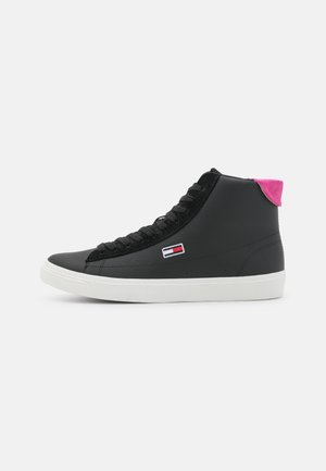 Baskets montantes noires avec semelle blanche, lacets noirs, petit logo rectangulaire rouge, blanc et bleu sur le côté, et languette rose au talon.