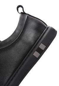 Scarpa nera slip-on con tomaia sintetica liscia, forma rotonda e suola testurizzata con un accento metallico sul lato.