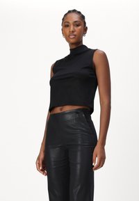 Čierny bezrukávový crop top s vysokým výstrihom, vyrobený z hladkej látky, kombinovaný s čiernymi koženými nohavicami s vysokým pásom.