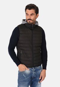 Gilet imbottito nero con chiusura a zip e tasche laterali. Foderato con cappuccio grigio, presenta una texture trapuntata e uno stile aderente.