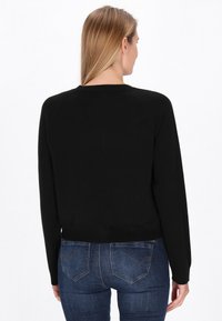 Mustahdollinen musta neulepusero pitkillä hihoilla, pyöreällä kaula-aukolla ja lyhyellä leikkauksella, yhdistettynä tummansinisiin farkkuihin, joissa on takataskujen ompeleet.
