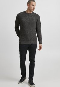Dark gray knitted sweater with a crew neck, textured pattern, and long sleeves. Worn with black slim-fit pants and black sneakers.