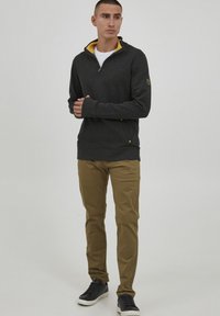 Sudadera gris con cremallera y forro amarillo, de mangas largas y bolsillos laterales, combinada con pantalones color marrón claro y zapatillas negras. Diseño sencillo.