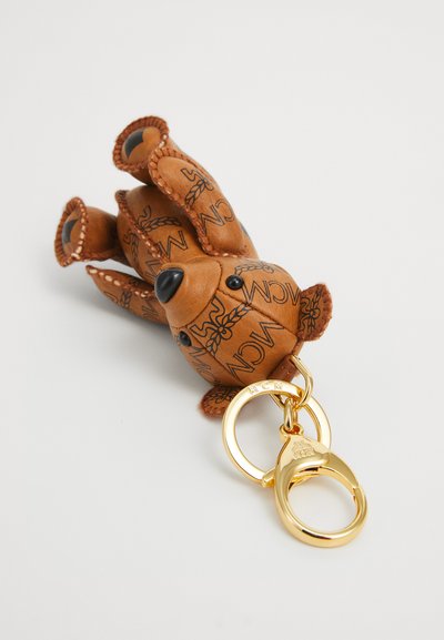 Bruine leren teddybeer sleutelhanger met zwarte logo's en gouden metalen ring en sluiting op een witte achtergrond.
