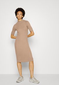 Vestido midi bege de manga curta feito de tecido canelado, com um decote alto e silhueta justa ao corpo, combinado com sapatilhas cinza claro.