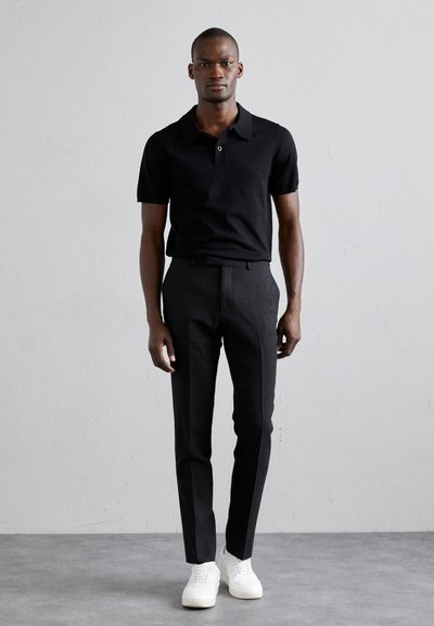 Svart polo med knapper, sammen med slim-fit svarte bukser og hvite joggesko, som viser en minimalistisk design.