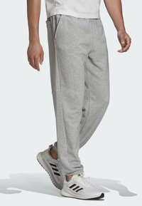 Graue Baumwoll-Sweatpants mit Seitentaschen, schmal zulaufenden Beinen und elastischem Bund, kombiniert mit weißen Turnschuhen mit schwarzen Streifen.