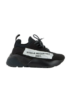 Baskets noires de sport avec semelle épaisse, détails texturés et étiquette blanche sur le côté indiquant "STELLA MCCARTNEY 2001" avec fermeture à lacets.