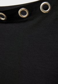 Schwarzer Stoff mit drei silbernen Metallösen entlang der oberen Kante, der Textur und leichte Falten im Material zeigt.