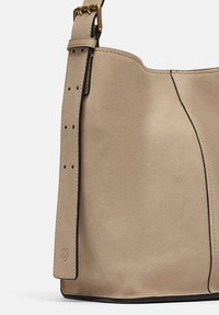 Borsa a tracolla in suede beige con una texture morbida, una forma distintiva, una tracolla regolabile e un accento nero lungo il bordo.