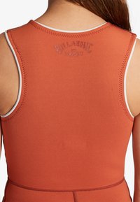 Verbrande oranje wetsuit met witte afwerking, met een ronde hals en gestikte details. Billabong-logo in reliëf op de achterkant.